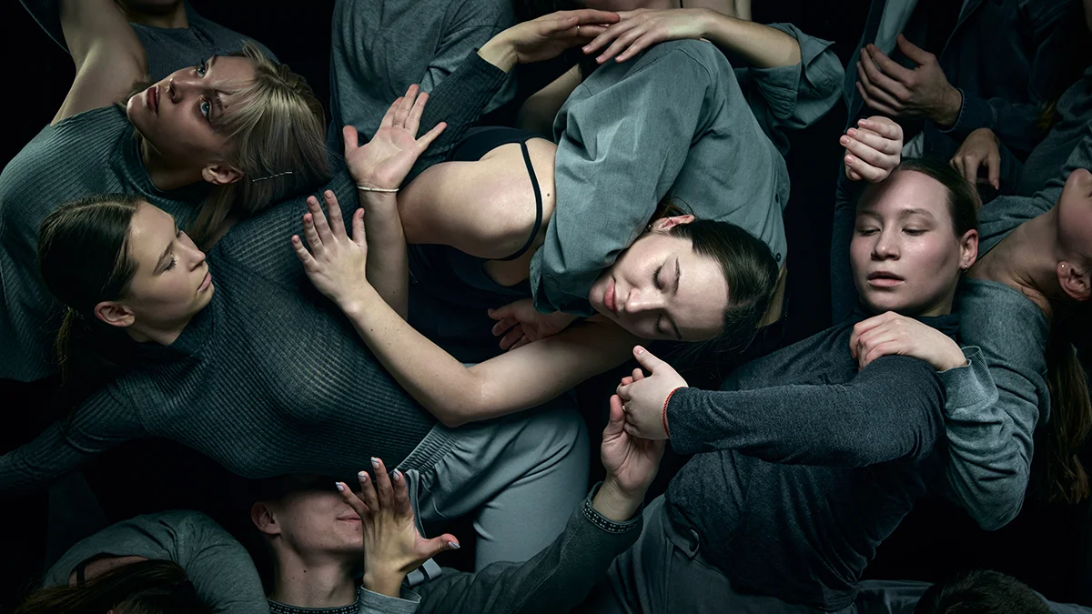 A closely knit social network of support with a bird perspective of multiple dancers embracing one another on a dark stage